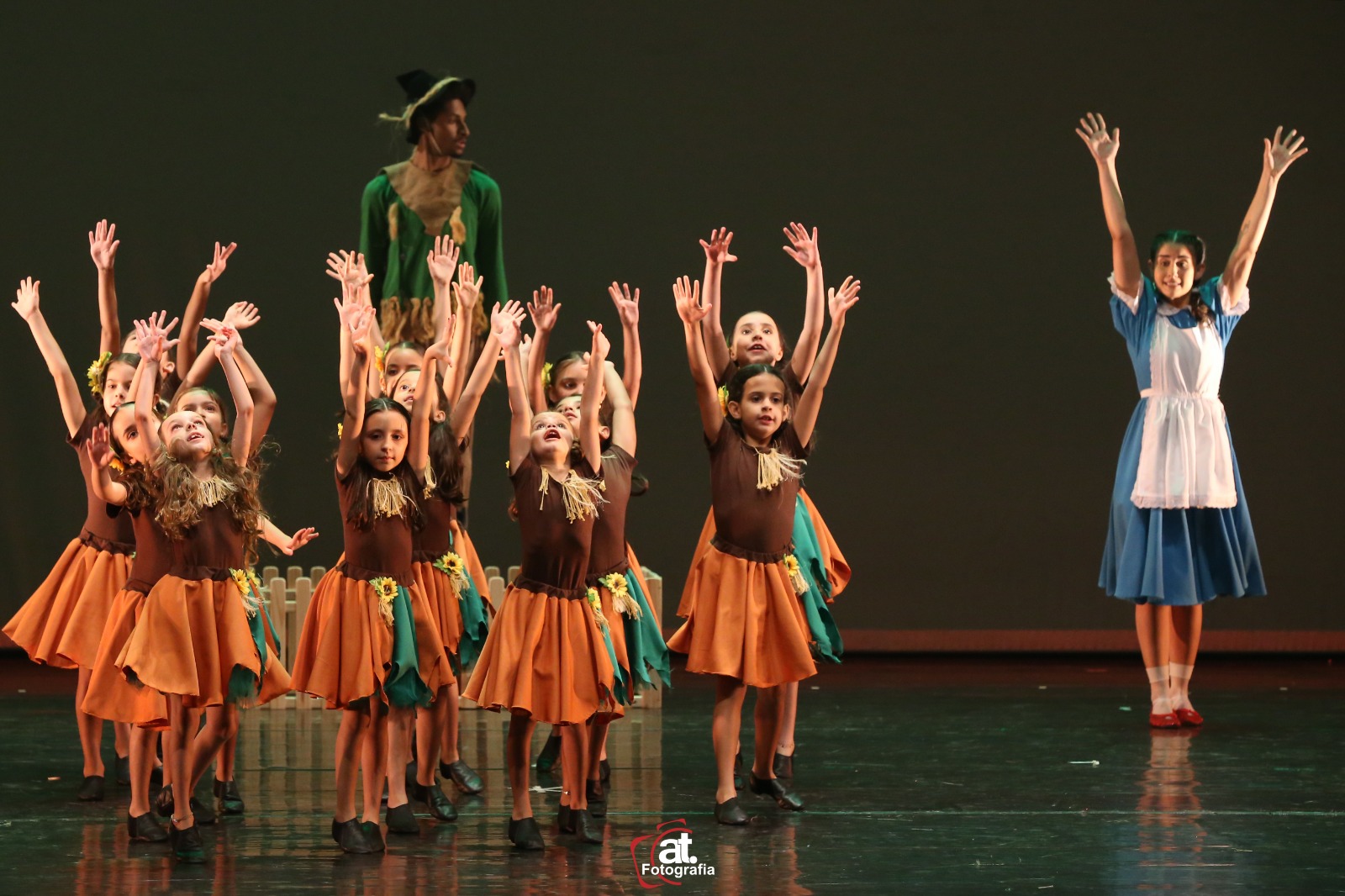 Turma de alunas com os braços erguidos em cena